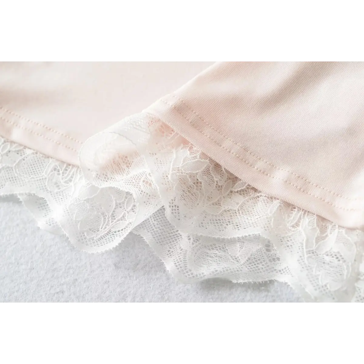 Close-up of the layered lace hem on a light pink cami top, showing the intricate floral pattern.