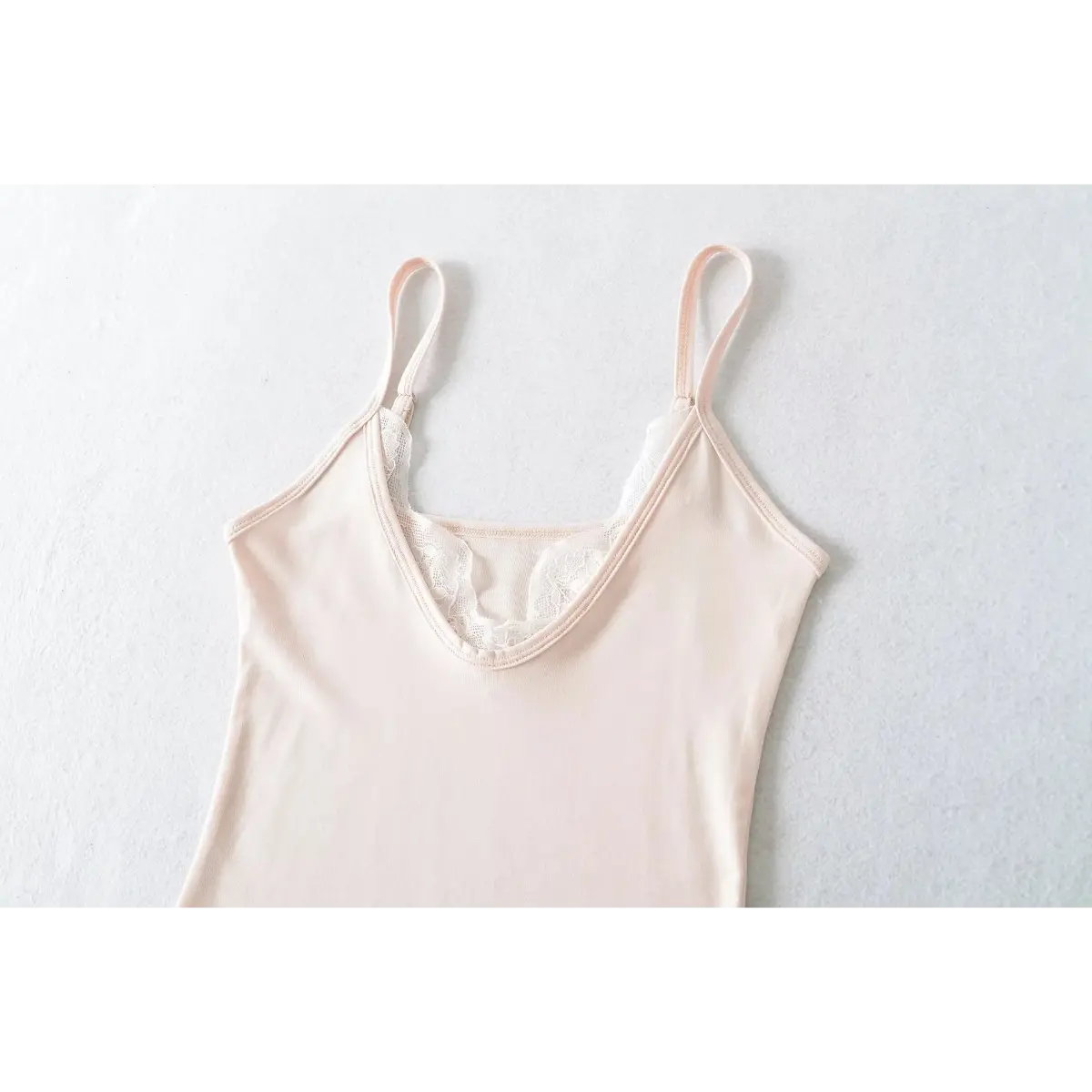 Full front view of a light pink cami top, featuring a V-neck with lace trim and adjustable spaghetti straps.