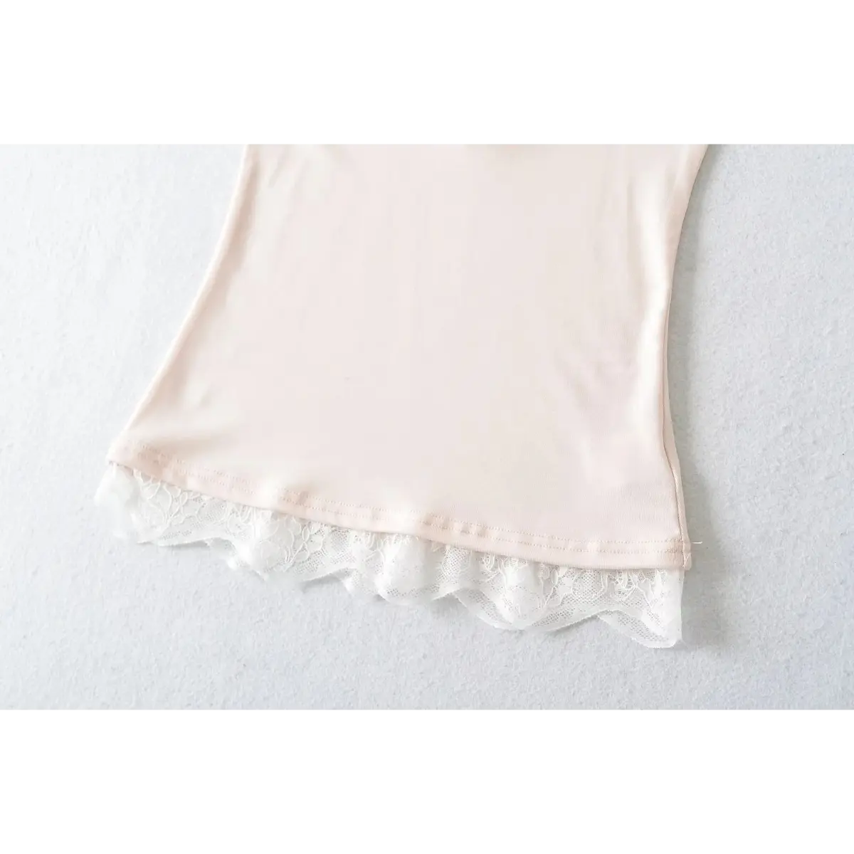 Close-up of the scalloped lace hem on a light pink cami top, showing the intricate floral pattern and stitching.