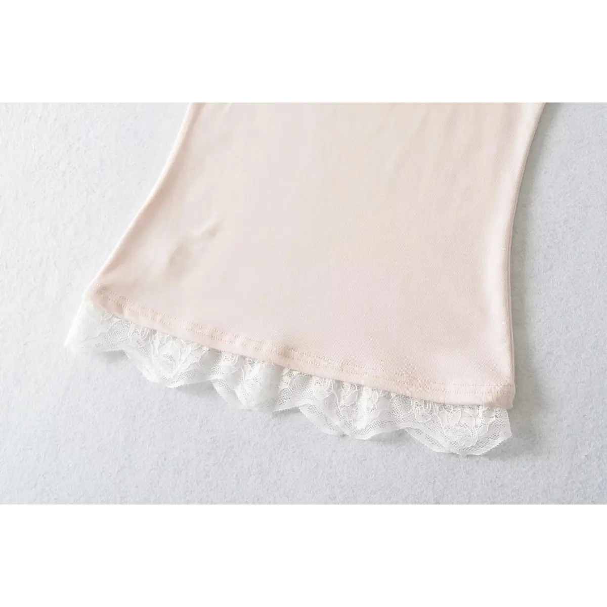 View of the hem on a light pink cami top, showcasing layered white lace trim with a scalloped edge.