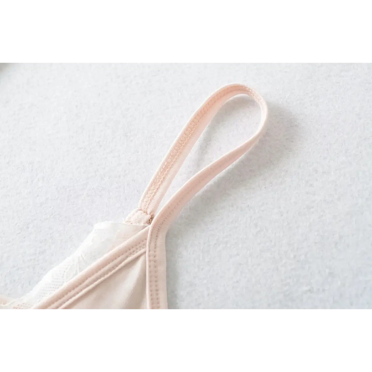 Close-up of the adjustable spaghetti strap on a light pink cami top, highlighting the neat stitching and fabric texture.