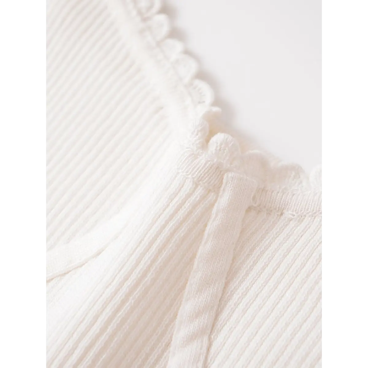 Close-up of the scalloped lace neckline on a white ribbed cami, highlighting the delicate knit construction.