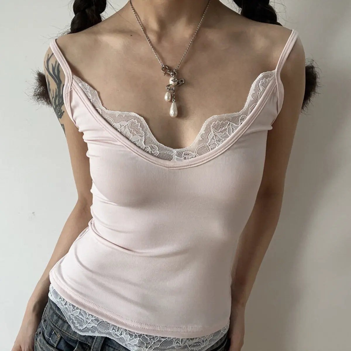 Form-fitting light pink ribbed cami top with white lace trim at the neckline and hem, styled with jeans.