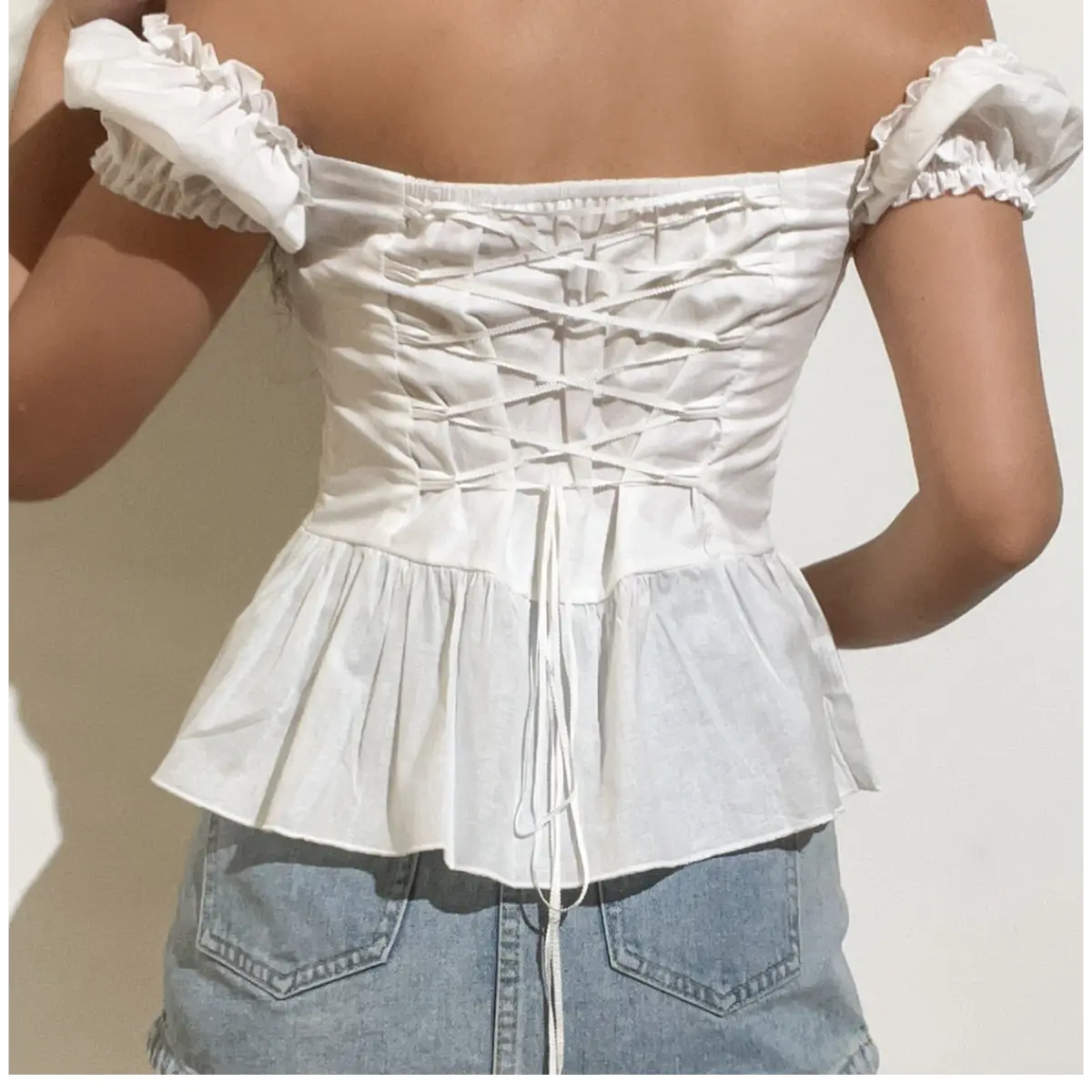 Back view of a white off-shoulder peplum top, focusing on the corset-style lace-up closure and adjustable drawstring.