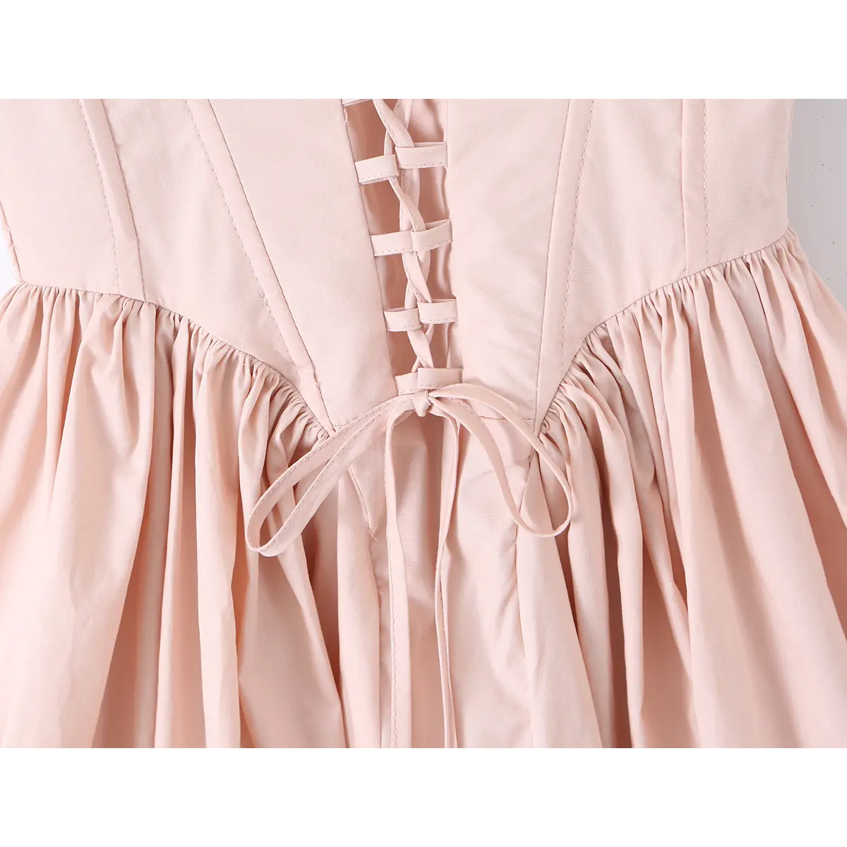 Close-up of the lace-up tie closure at the back waist of a light pink dress.