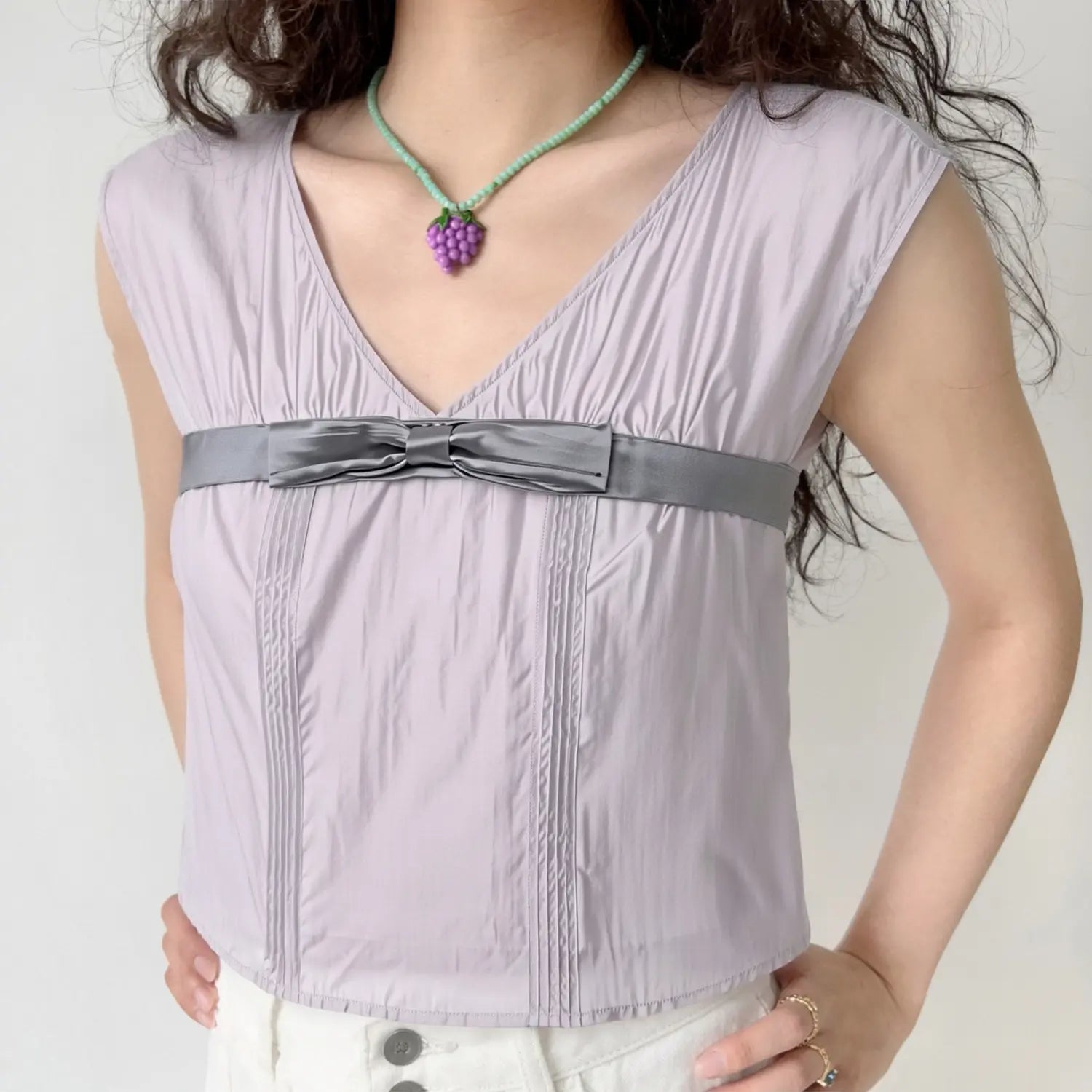 Lifestyle full model shot lavender gray waist bow sleeveless camisole, hidden V neck, vertical pin-tuck pleats, wide cap sleeves, match with white high waist wide leg pants, soft gentle daily casual styling