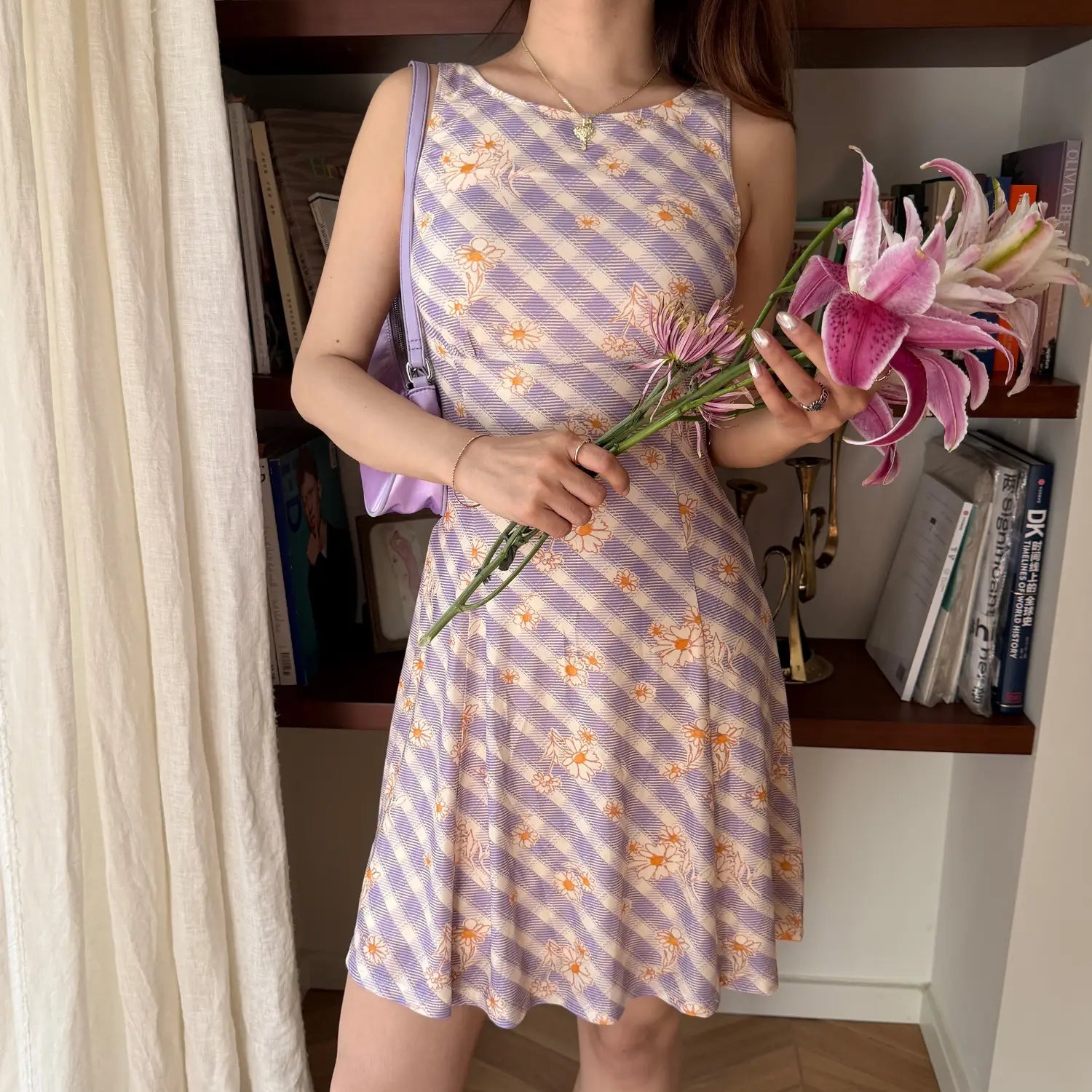  Lifestyle shot of a woman in a lavender checkered daisy print dress, holding a bouquet of pink lilies