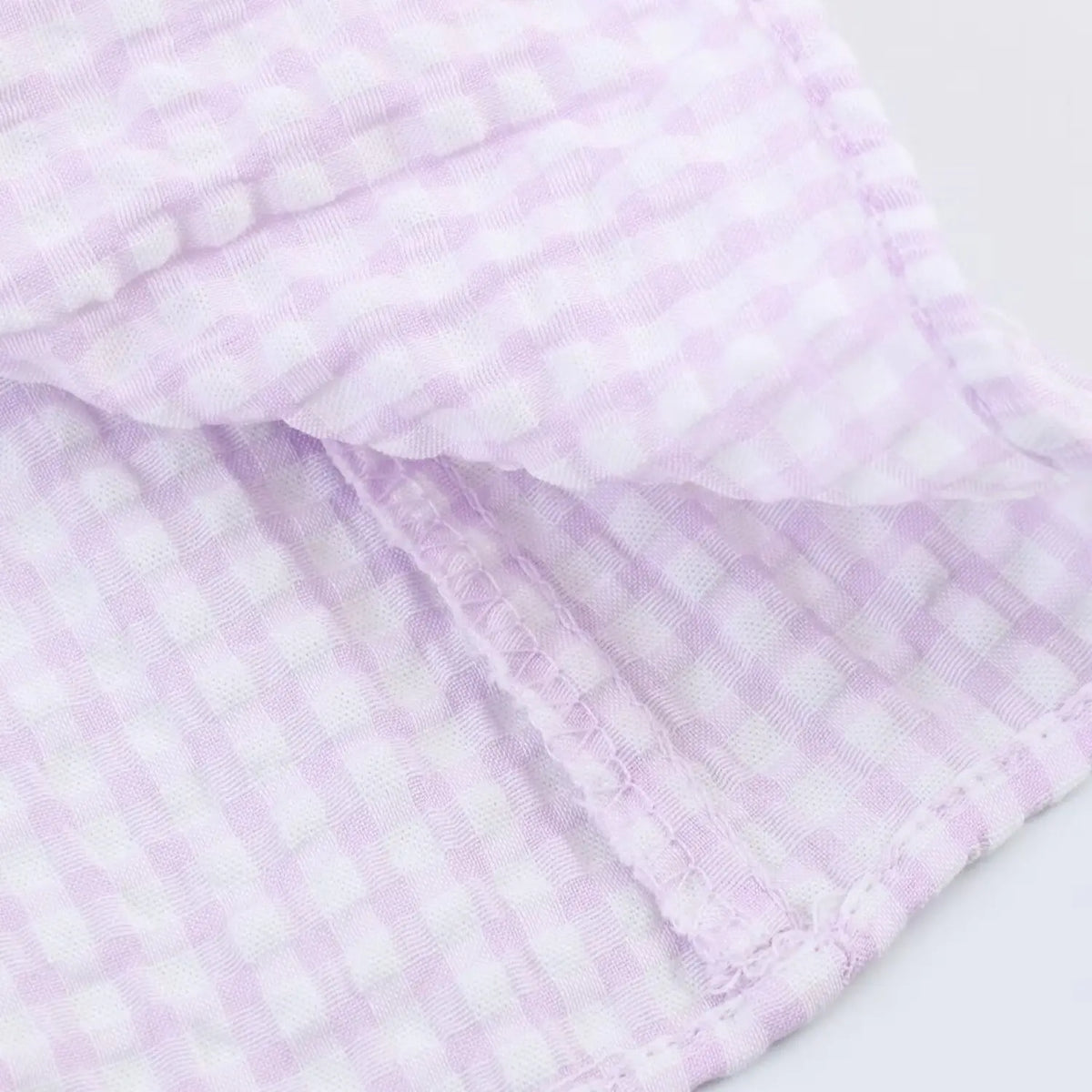 Close-up inner seam stitching, lavender gingham textured fabric, reinforced garment seams