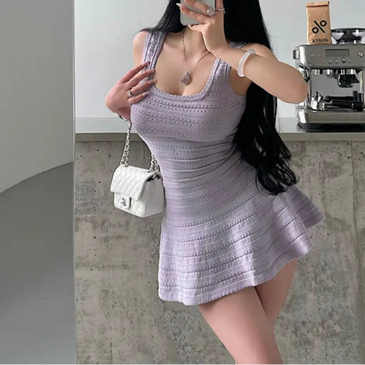 A woman wearing a lavender knit mini dress with a square neckline, textured pattern, and flared skirt, styled with a white bag.

