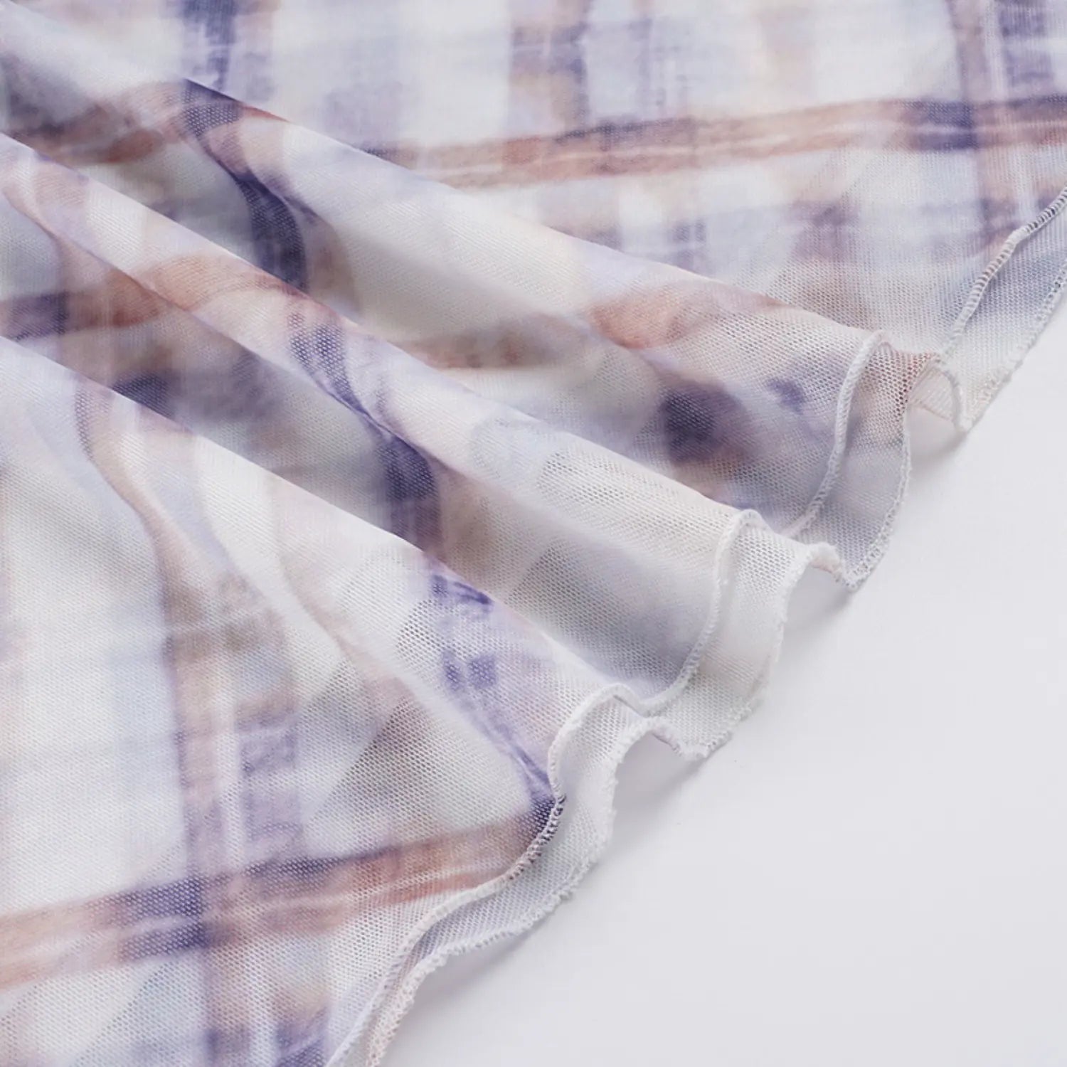 Macro close texture shot of lightweight sheer mesh skirt fabric with muted purple & tan watercolor plaid, showcasing neat wavy elastic overlock stitching along raw hem edge