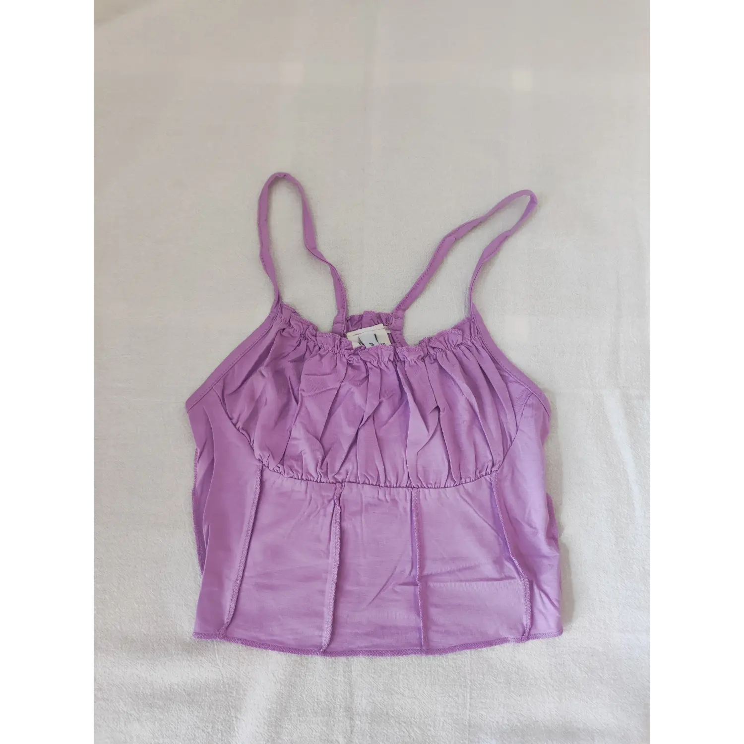 Flat lay front view lavender ruffle neck ruched bust cami crop top on white textured fabric