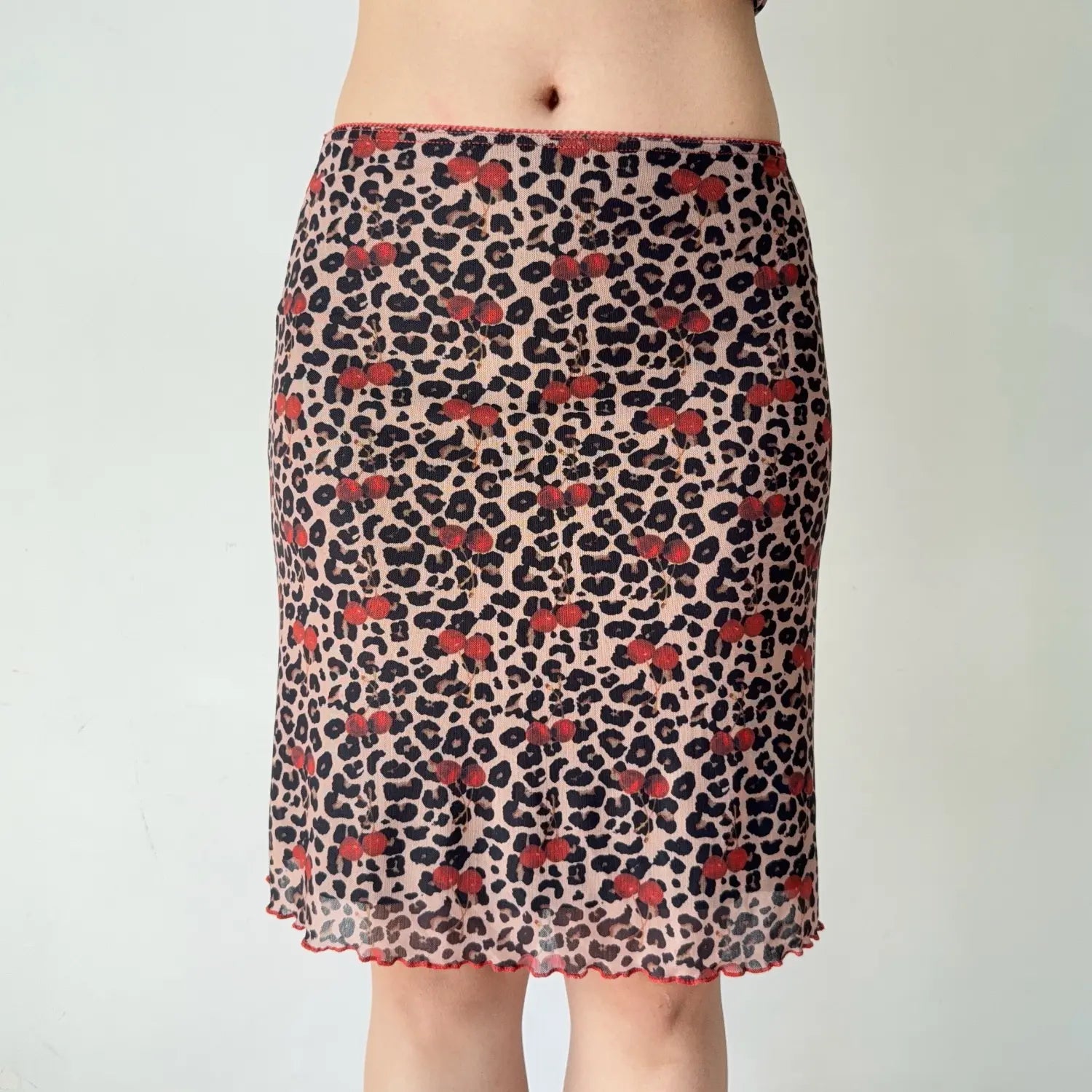 Detail shot of matching mesh midi skirt, high waist, allover leopard cherry pattern, red lettuce ruffle bottom hem