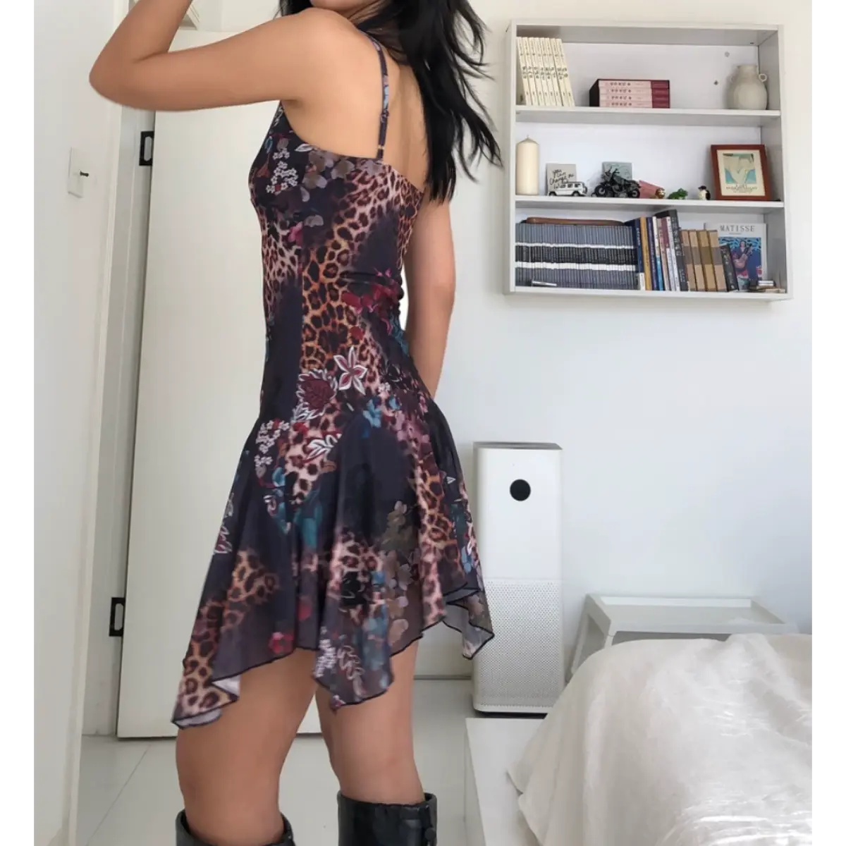 Back view of a woman wearing a form-fitting mesh mini dress with a dark leopard and floral print, showing the thin spaghetti straps and asymmetrical ruffled hem.