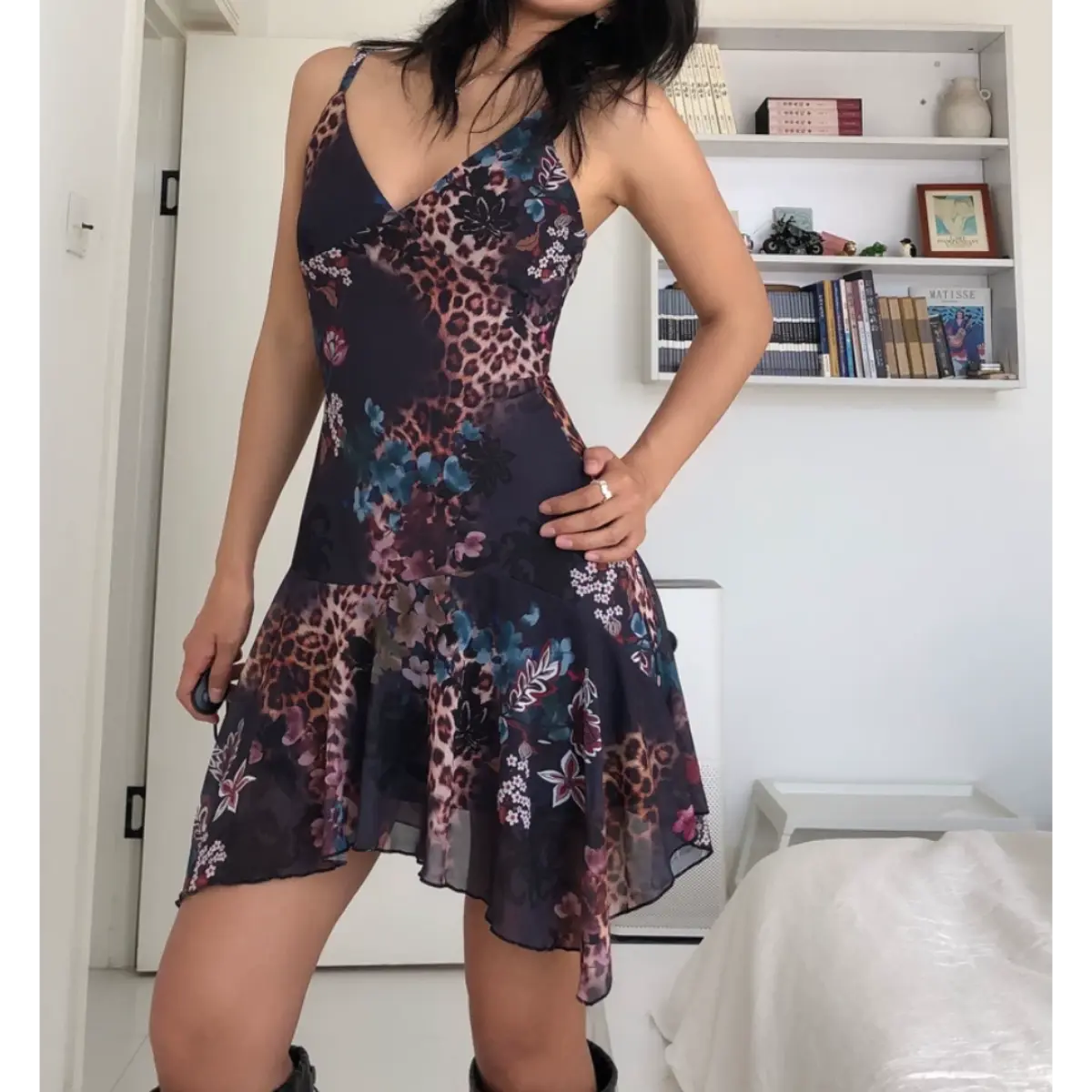 Side view of a woman wearing a form-fitting mesh mini dress with a dark leopard and floral print, showing the fitted bodice and asymmetrical ruffled hem.

