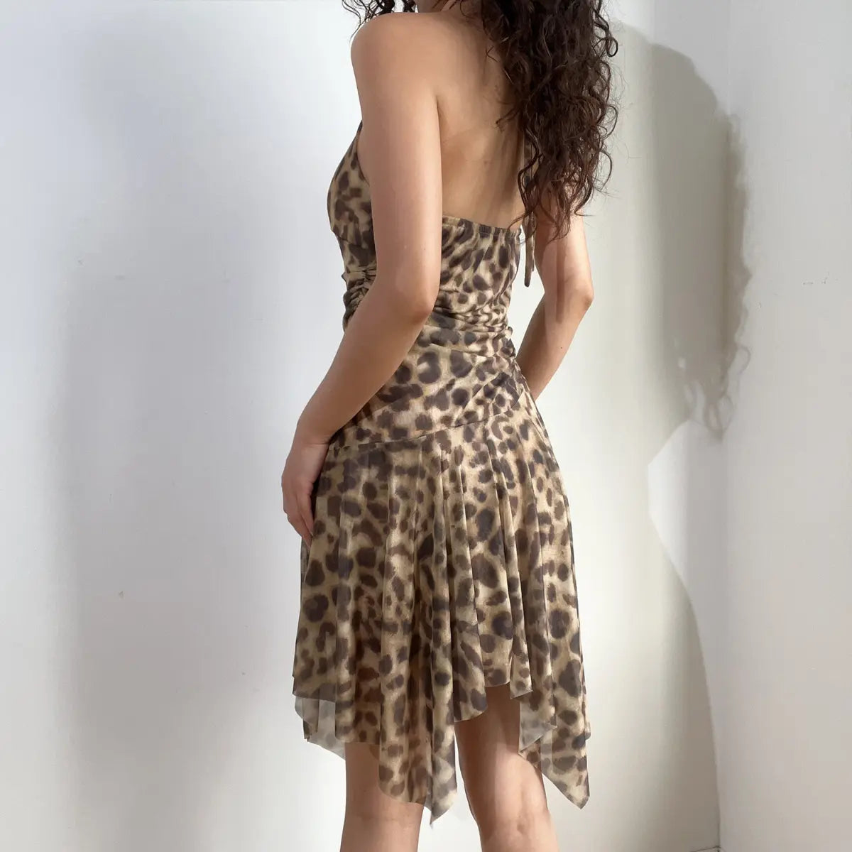 Back view of a leopard print halter dress, showcasing the open back, tie closure, and asymmetrical hemline.