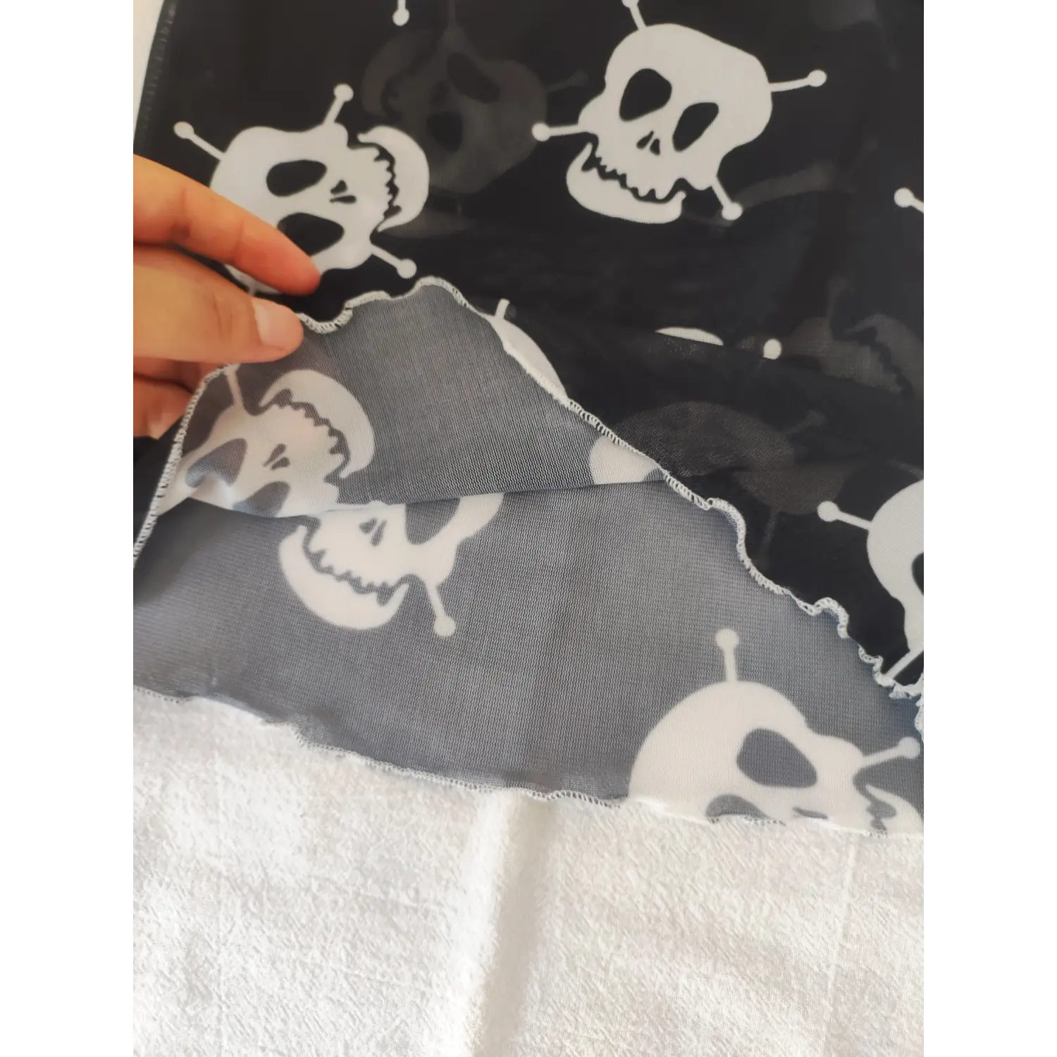 Closeup folded hem detail of goth cami top, wavy lettuce trim, stretch sheer mesh and skull print reverse side