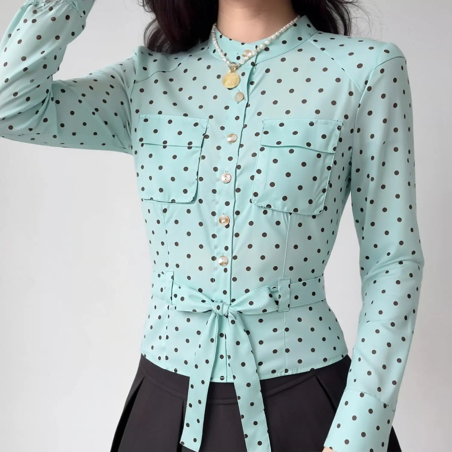 Lifestyle model shot light blue brown polka dot stand collar long sleeve shirt, dual chest patch pockets, self fabric waist tie belt, fitted cropped silhouette