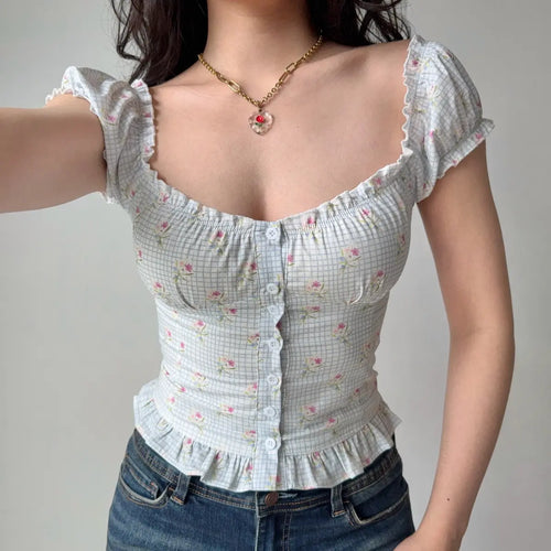 Front view of a woman wearing a light blue checkered floral puff-sleeve top, featuring a sweetheart neckline, center buttons, and ruffled hem.