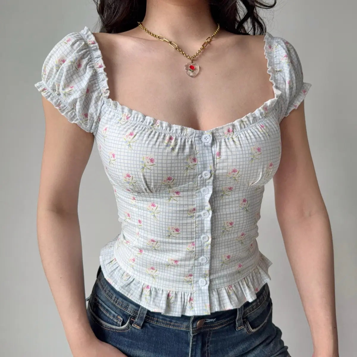 Full front view of a light blue checkered floral puff-sleeve top, showcasing the sweetheart neckline, button placket, and ruffled peplum hem.