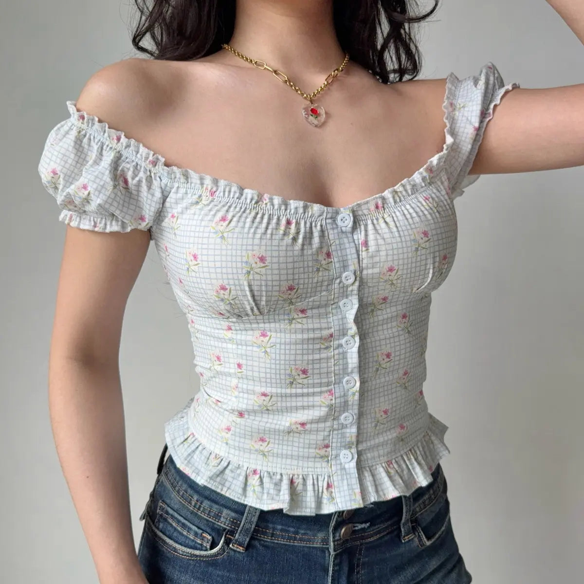Woman wearing a light blue checkered floral puff-sleeve top styled off the shoulder, highlighting the elasticized neckline and form-fitting silhouette.