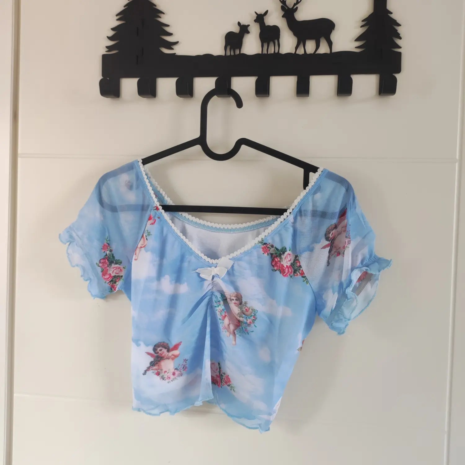 Hanging front view light blue v‑neck mesh crop top angel rose print displayed on black hanger