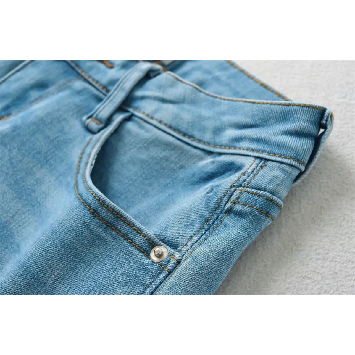 Close-up of the front pocket and stitching on light blue low-rise denim shorts.