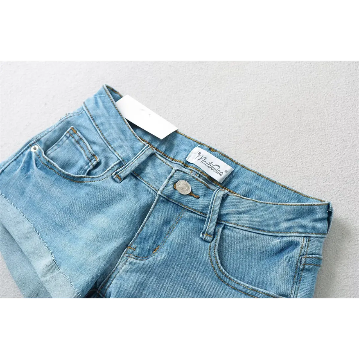 Close-up of the waistband and label on light blue low-rise denim shorts.