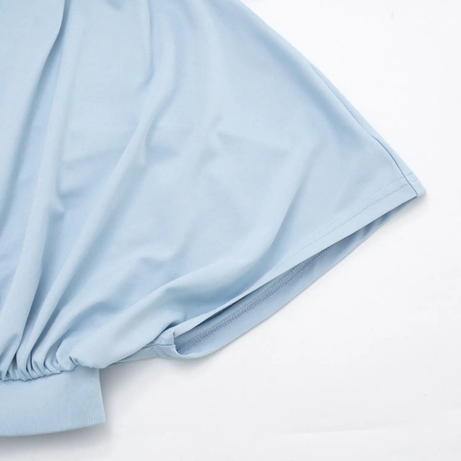 Close-up detail of dolman short sleeve cuff, sky blue soft jersey fabric, neat double parallel straight stitching along sleeve hem, loose flowy batwing sleeve silhouette