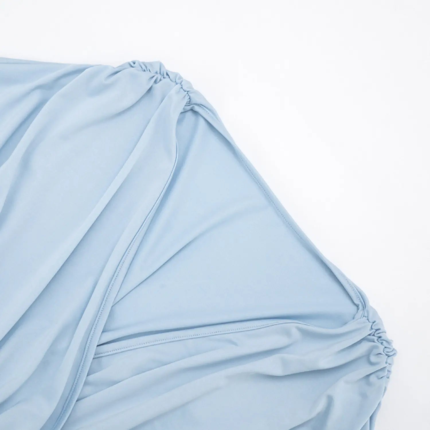 Top-down flat partial shot of wrap crop top shoulder construction, dual side shoulder ruched gathers, sky blue drapey jersey fabric, neat enclosed edge stitching, loose flowy batwing sleeve silhouette