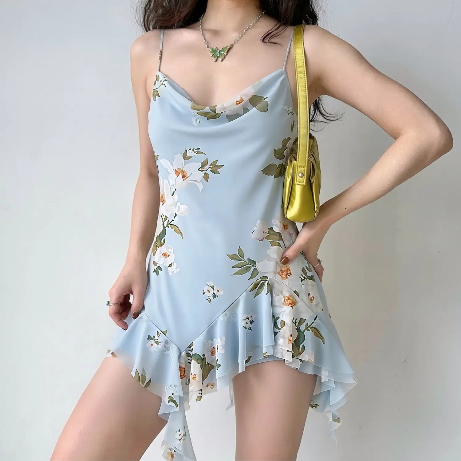 Model wearing light blue floral cowl neck slip mini dress, thin spaghetti straps, asymmetrical ruffled streamer hem, vintage white flower print