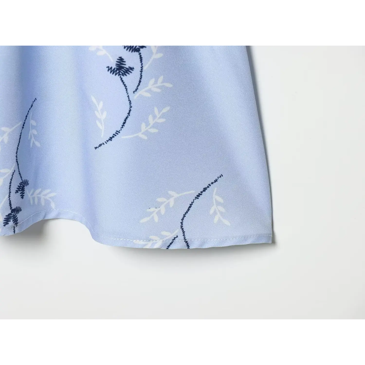 Close‑up finished stitching hem detail of light blue floral mini dress