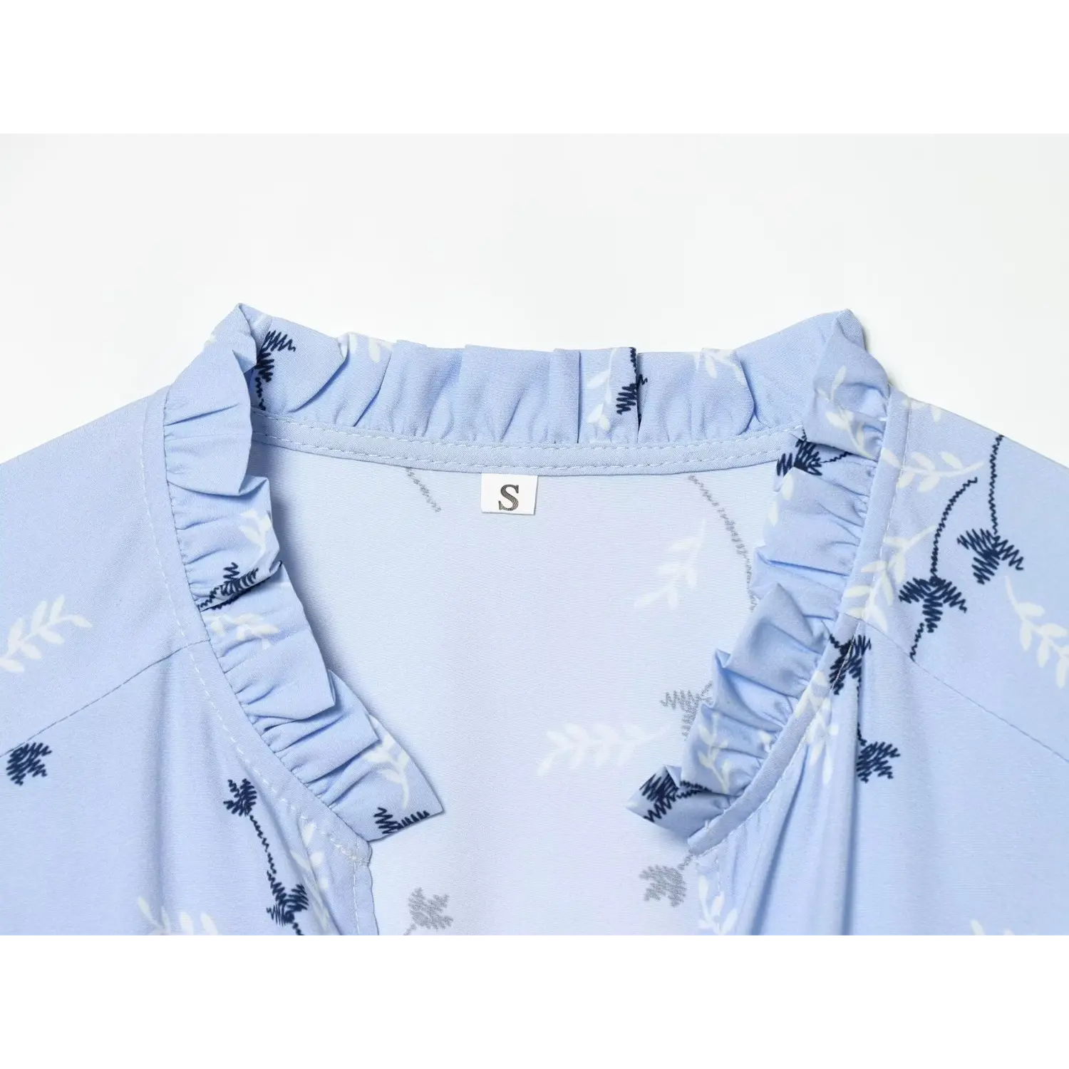 Macro close‑up of ruffle v‑neck collar, inner size label and floral print fabric