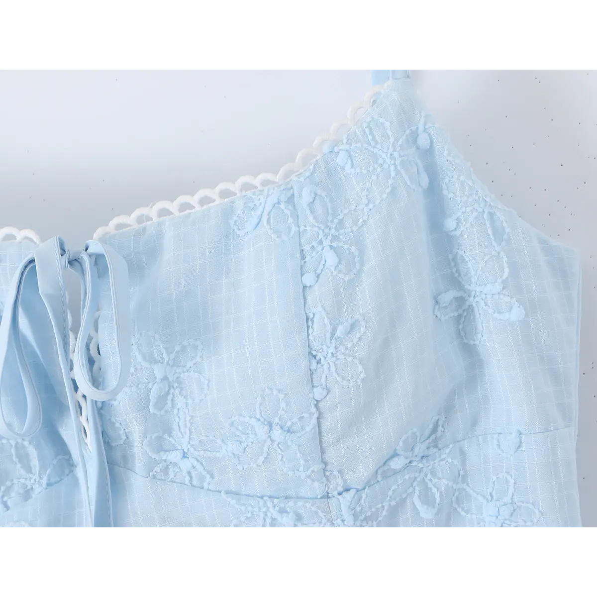 Close-up of the keyhole tie, lace trim, and floral embroidery on the bodice of a light blue spaghetti strap dress.