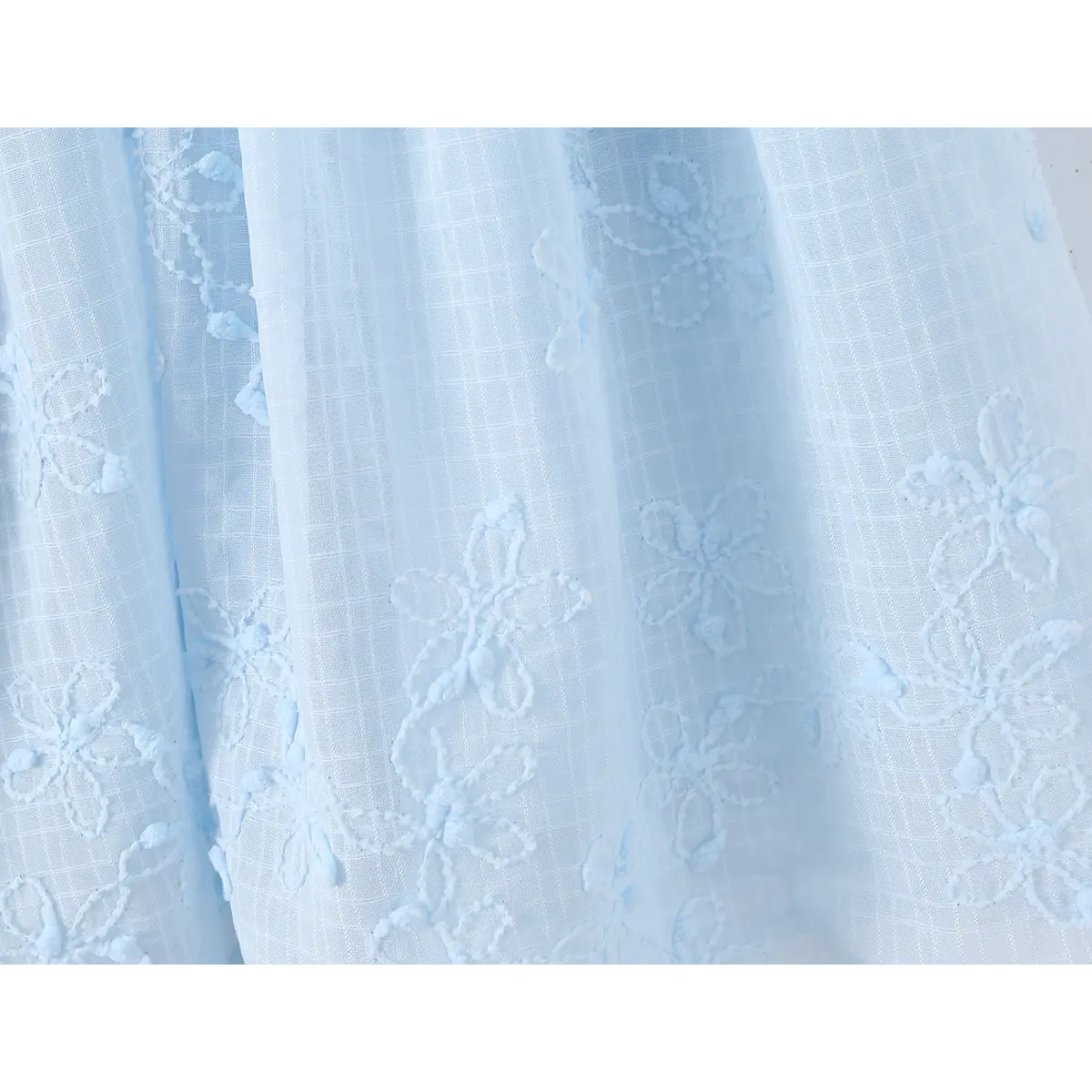 Close-up of the fabric texture and floral embroidery on the skirt of a light blue spaghetti strap dress.