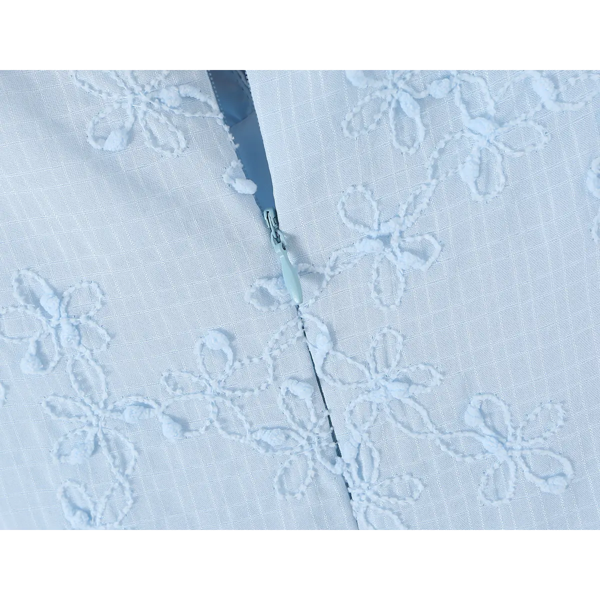 Close-up of the invisible zipper closure on a light blue spaghetti strap dress with floral embroidery.
