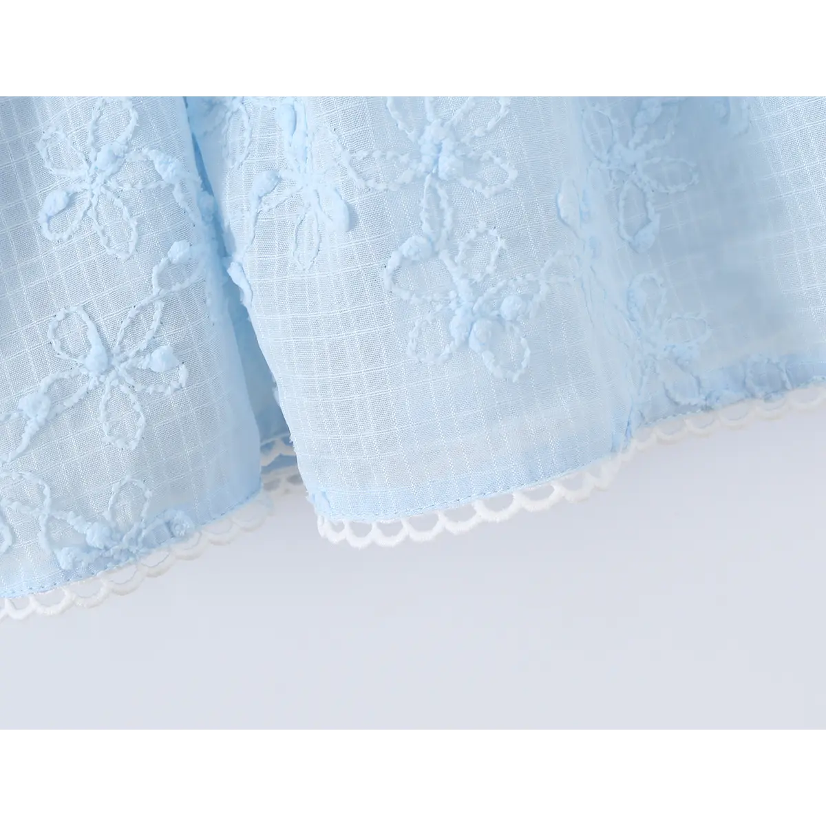 Close-up of the lace-trimmed hem and floral embroidery on a light blue spaghetti strap dress.