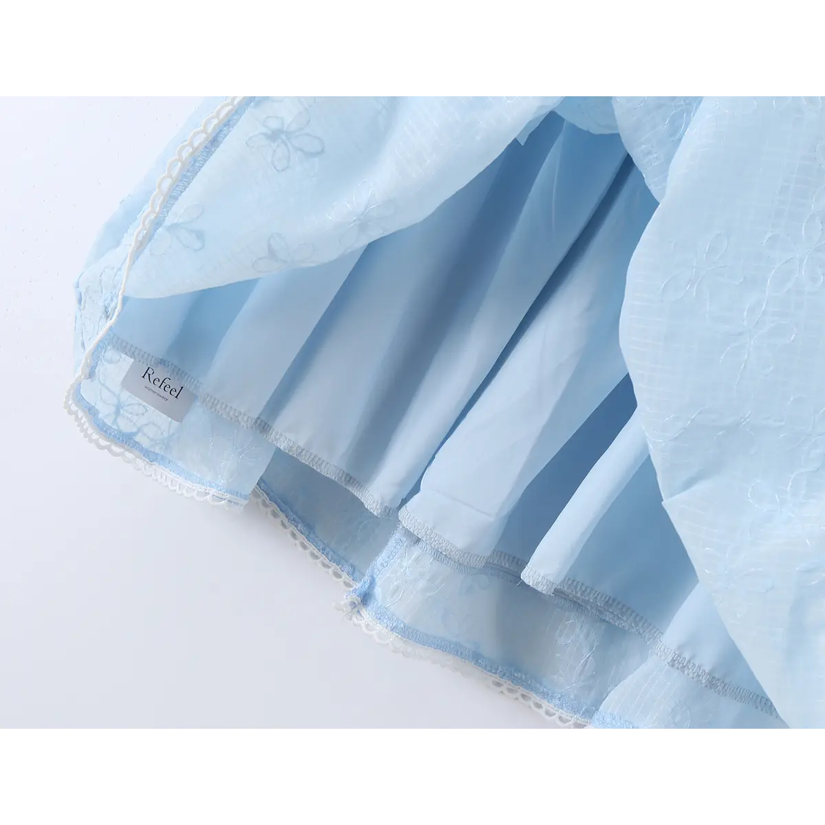 Close-up of the lining and label inside a light blue spaghetti strap dress with floral embroidery.