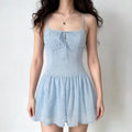 Full-body shot of a woman wearing a light blue spaghetti strap dress with floral embroidery, lace trim, and keyhole tie detail.