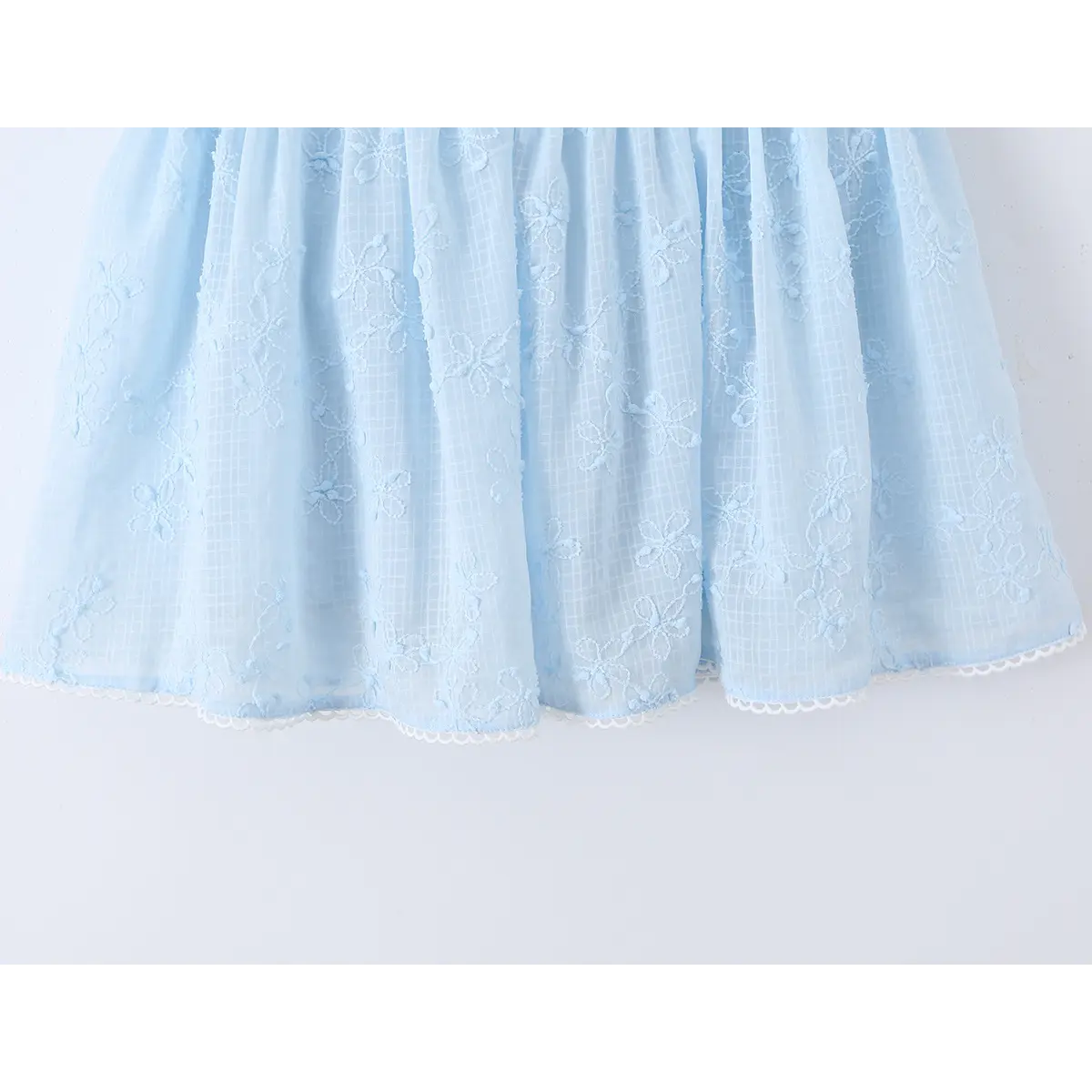 Close-up of the skirt hem on a light blue spaghetti strap dress with floral embroidery and lace trim.
