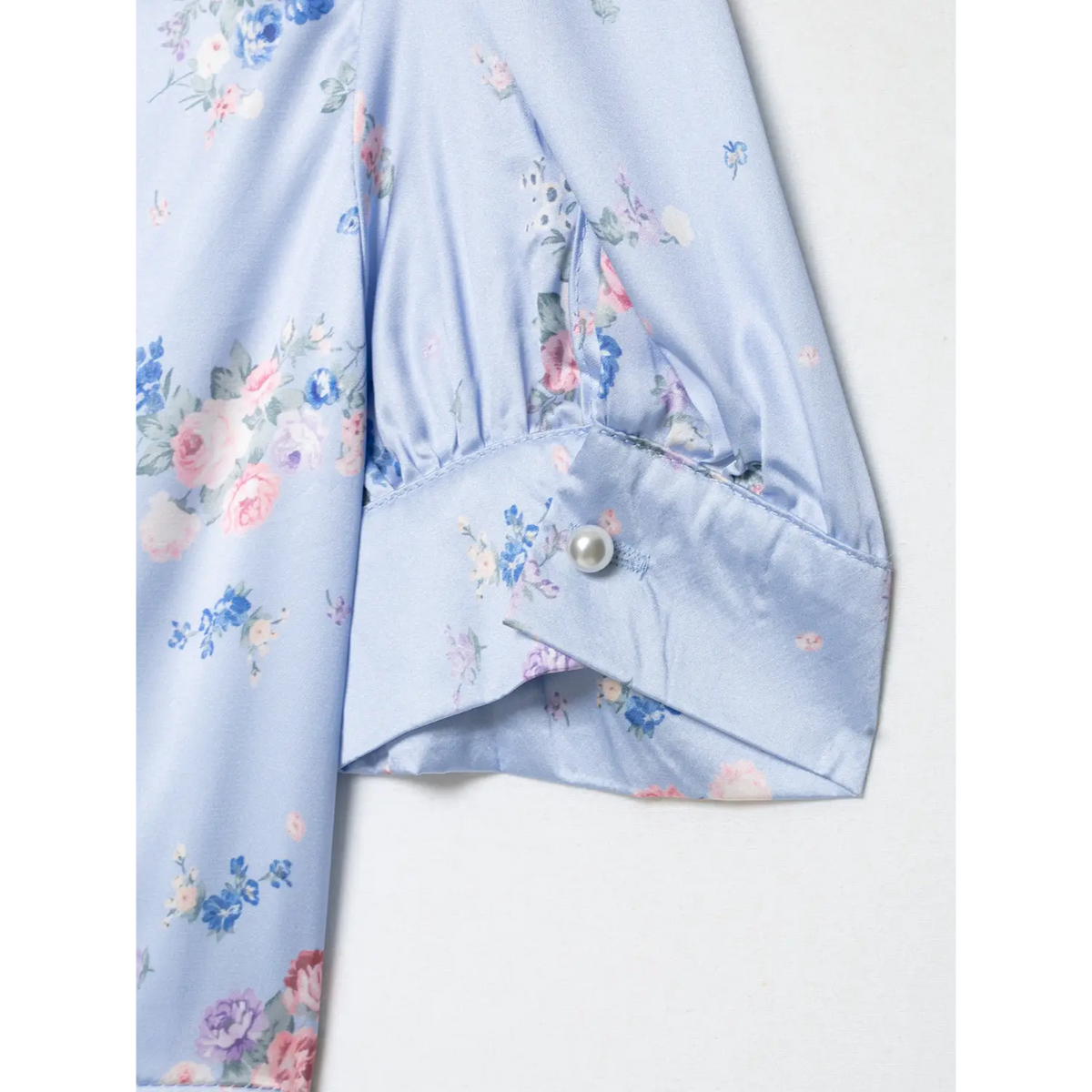 Close-up of puff sleeve cuff, decorated with round pearl button, light blue satin with floral print