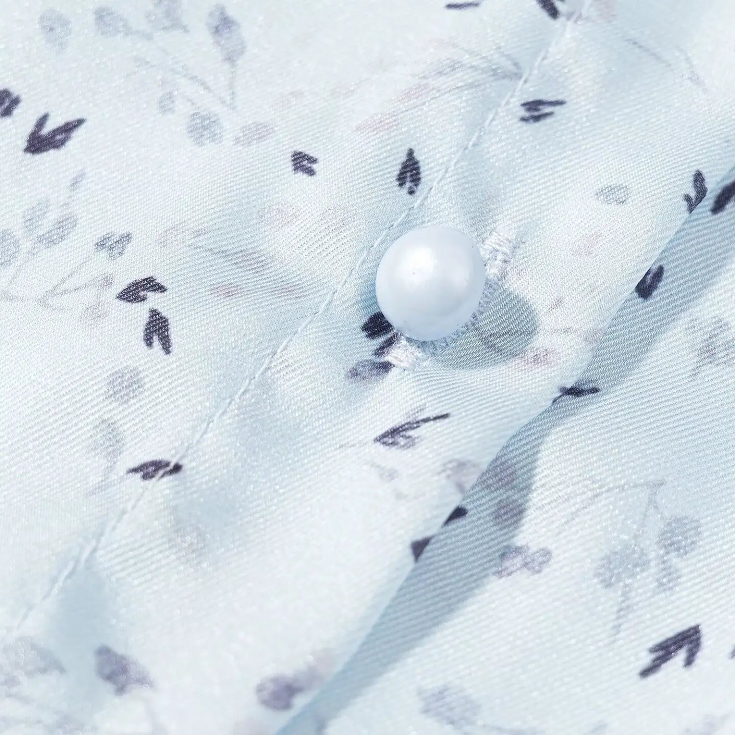 Macro close‑up round pearl decorative button on light blue ditsy floral printed fabric