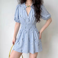 Female model wearing light blue floral print mini dress, front full body view, smocked waist, puff short sleeves