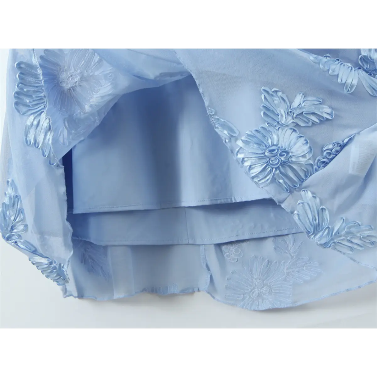 Close-up of the layered construction on a light blue gown, showing the mesh overlay, 3D floral embroidery, and smooth inner lining.