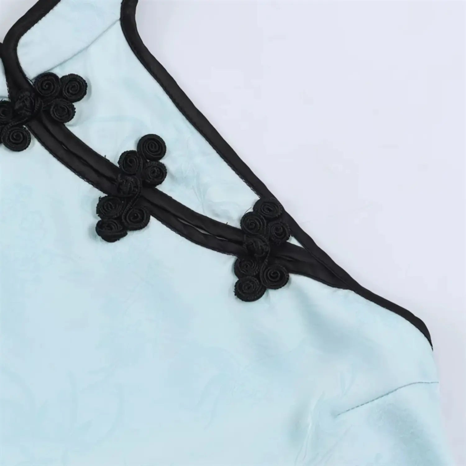 Extreme close-up black handmade floral chinese frog buttons, wrapped fabric knot detail, double black piping along diagonal placket