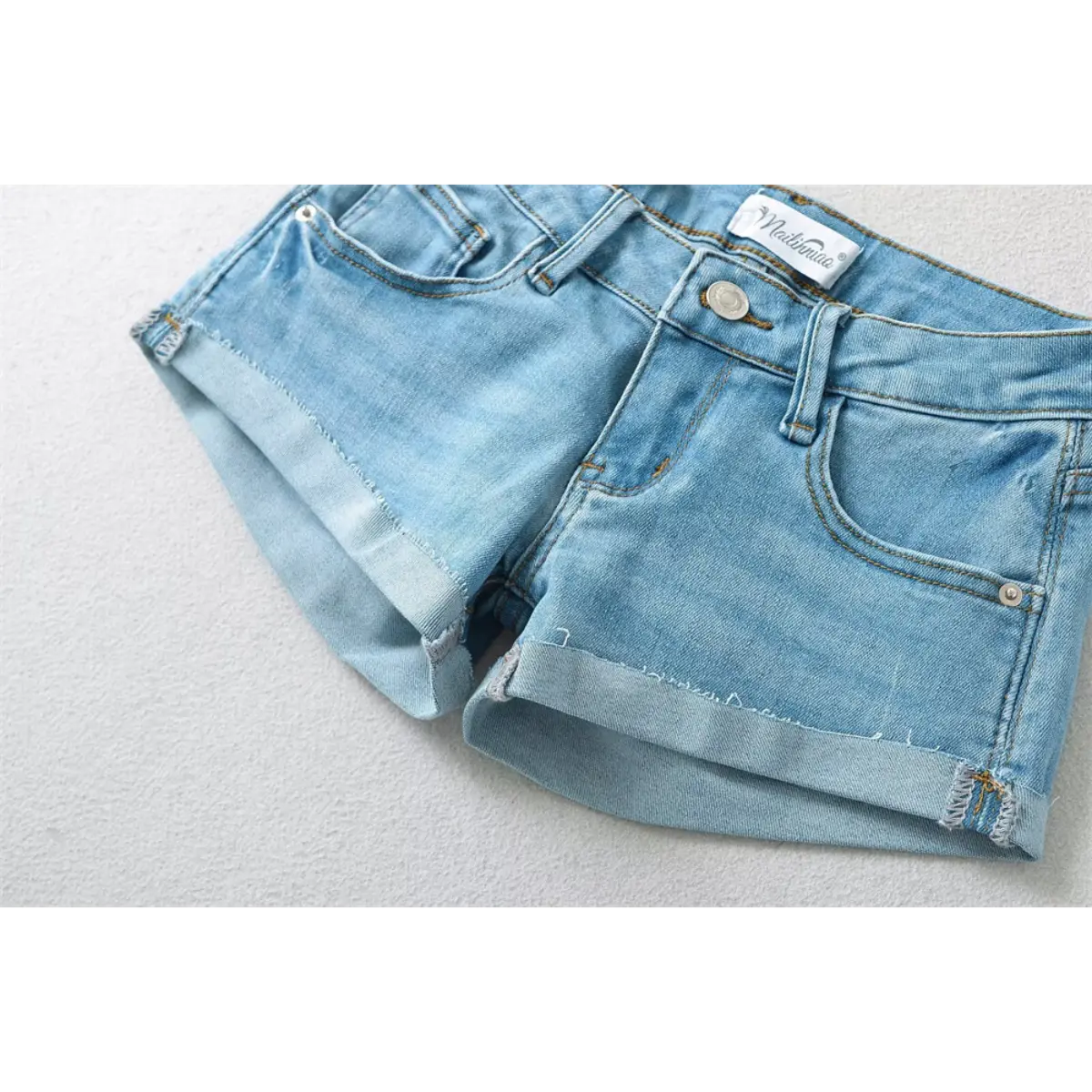 Close-up side view of light blue low-rise denim shorts, showing the rolled cuffs and stitching.