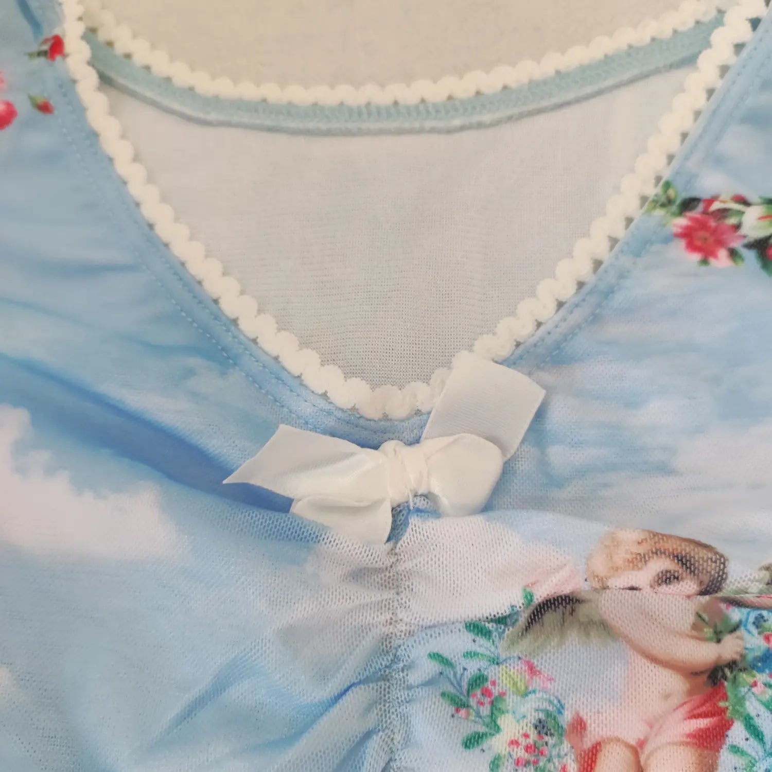 Close‑up v‑neckline white lace trim and front satin bow detail on light blue cherub print mesh crop top