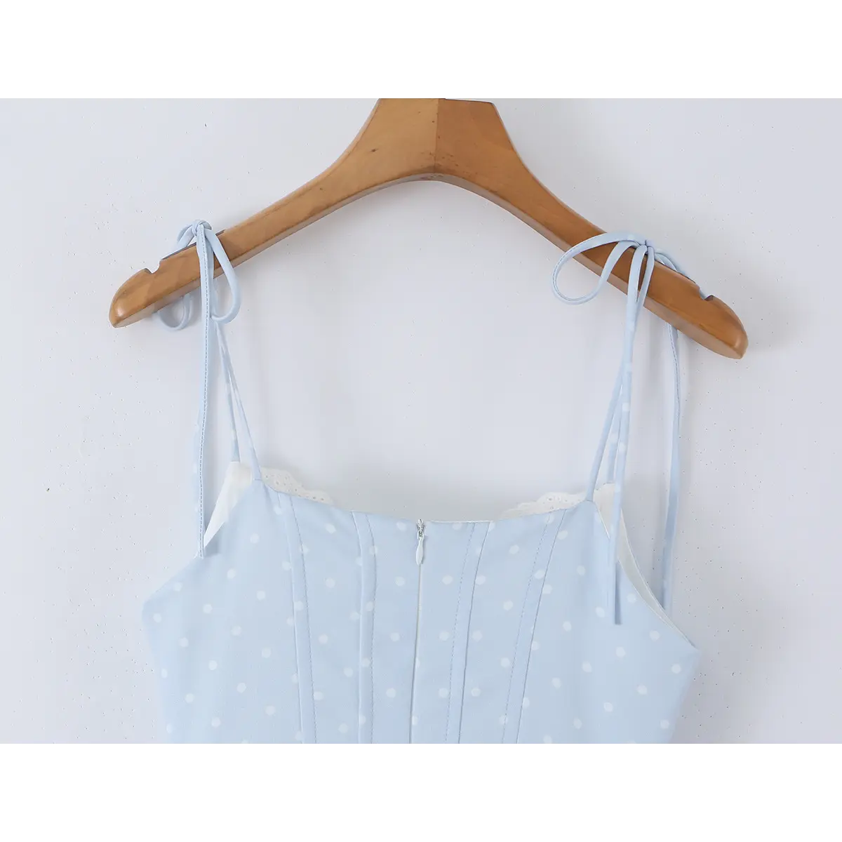 Back view of a light blue polka dot corset-style dress hanging on a wooden hanger, showing the zipper closure.