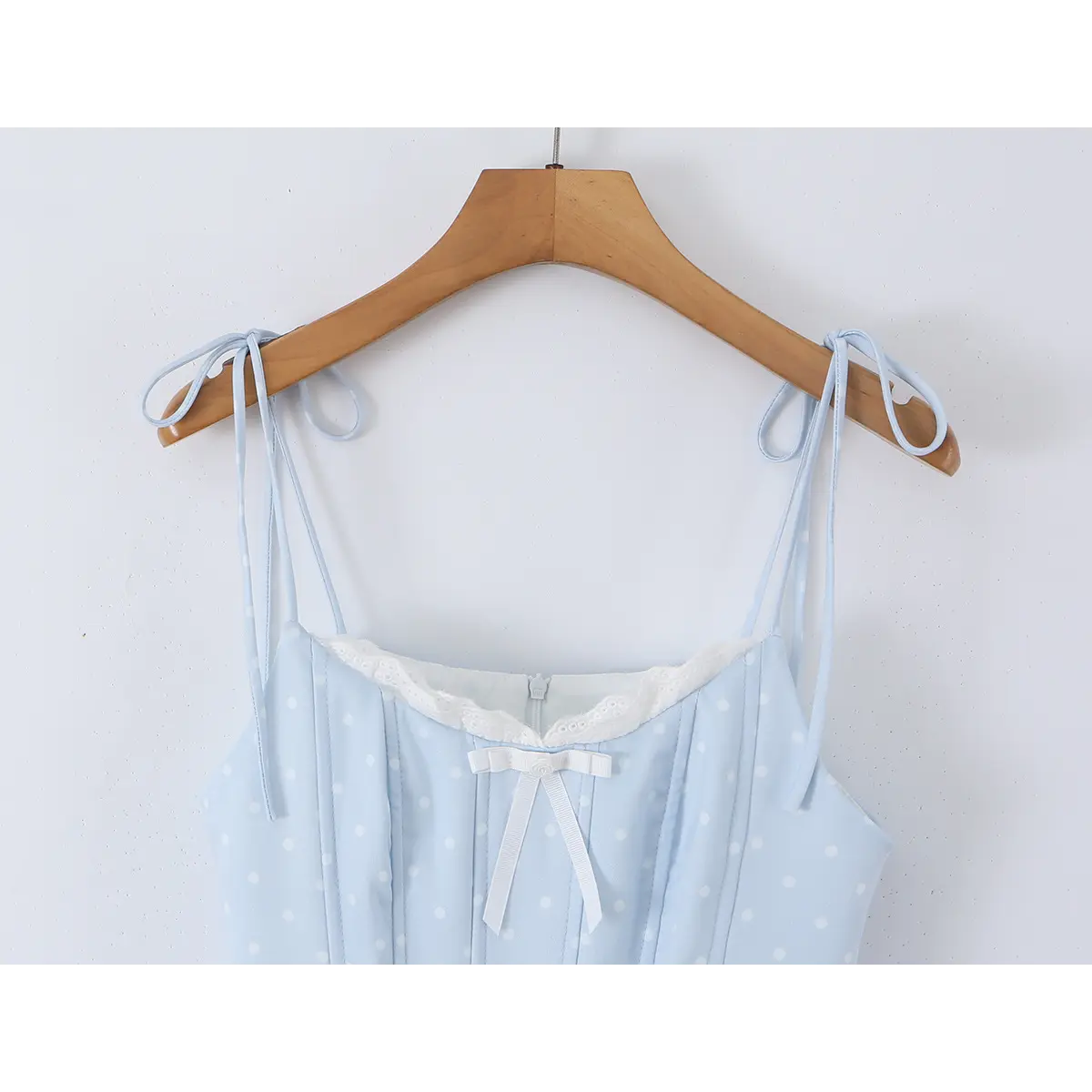 Close-up of the front bodice of a light blue polka dot dress, featuring lace trim and a white bow detail.