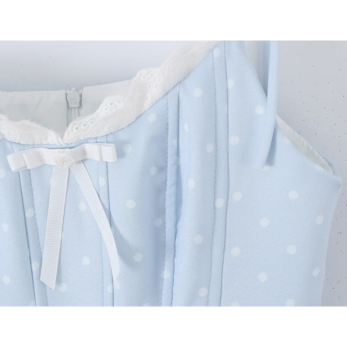  Close-up of the white bow and lace trim on the neckline of a light blue polka dot dress.