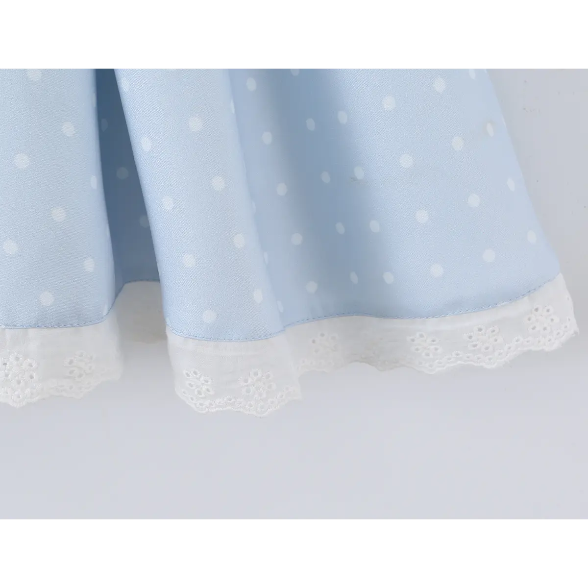 Close-up of the lace-trimmed hem on the flared skirt of a light blue polka dot corset-style dress.